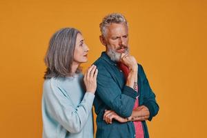 Sad senior couple standing together against orange background photo