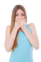 No more gossiping. Shocked young woman covering mouth with hands while standing isolated on white photo