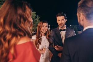 grupo de personas en ropa formal comunicándose y sonriendo mientras pasan tiempo en una fiesta de lujo foto