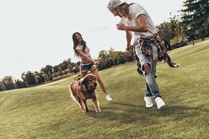 buen tiempo juntos. toda la longitud de una joven pareja moderna jugando con su perro mientras pasa tiempo sin preocupaciones en el parque foto