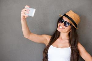 Selfie time. Joyful young women making selfie by her smart phone and smiling while standing against grey background photo
