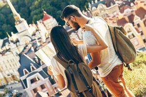 Beautiful young couple of tourists examining map while standing outdoors photo