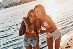 tiempo para relajar a dos mujeres jóvenes atractivas en traje de baño sonriendo mientras pasan tiempo sin preocupaciones en la playa foto