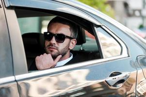 On the way to success. Thoughtful young businessman holding hand on chin while riding inside his car photo