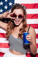 la libertad está en sus venas. hermosa joven dando paz y sosteniendo una lata mientras se enfrenta a la bandera nacional americana foto