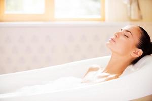 True bliss. Side view of attractive young woman keeping eyes closed while enjoying luxurious bath photo