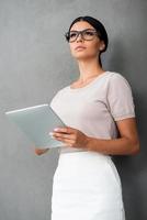 Nacido para liderar. vista de ángulo bajo de una joven empresaria segura de sí misma sosteniendo una tableta digital mientras se enfrenta a un fondo gris foto