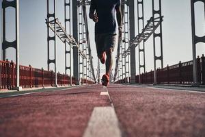 empujando al límite. Cerca de un joven africano vestido con ropa deportiva haciendo ejercicio mientras trotaba en el puente al aire libre foto