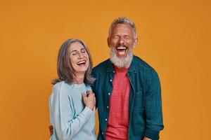 Beautiful senior couple laughing while standing together against orange background photo