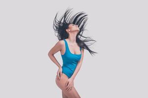 Beauty in motion. Attractive young woman in blue swimsuit keeping eyes closed while standing against grey background photo