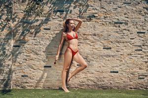 Full length of attractive young woman in bikini looking away and smiling while standing outdoors photo