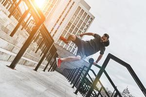 desafiándose a sí mismo. toda la longitud de un joven apuesto con ropa deportiva saltando sobre la barandilla mientras hace ejercicio afuera foto