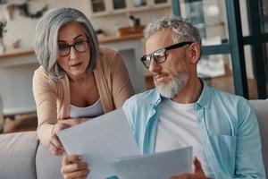 Concentrated senior couple in casual clothing taking care of their finances while bonding together at home photo