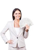 exitoso y rico. joven empresaria confiada en traje mostrando dinero y sonriendo mientras está de pie contra el fondo blanco foto