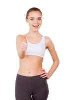 Sporty woman. Beautiful young woman in sports clothing showing her thumb up and smiling while standing isolated on white photo