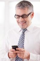 Typing a business message. Cheerful senior man in shirt and tie holding a mobile phone and smiling photo