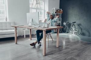 teniendo en cuenta el siguiente paso. apuesto joven mirando el monitor de la computadora y manteniendo las manos detrás de la cabeza mientras se sienta en su lugar de trabajo en la oficina creativa foto