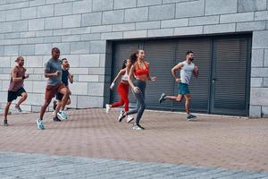 Group of young people in sports clothing jogging while exercising on the sidewalk outdoors photo