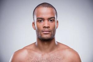 Pure masculinity. Portrait of young shirtless African man looking at camera while standing against grey background photo