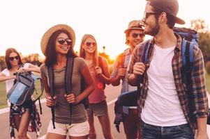 la libertad está en sus venas. grupo de jóvenes con mochilas caminando juntos por la carretera y luciendo felices foto