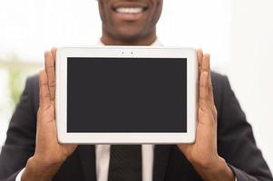 Copy space on his tablet. Cropped image of cheerful young African man in formalwear showing a screen of digital tablet and smiling at camera photo