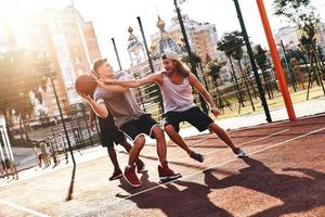 feliz de jugar grupo de jóvenes vestidos con ropa deportiva jugando baloncesto y sonriendo mientras pasan tiempo al aire libre foto