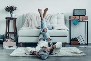 Spending carefree time. Beautiful young woman in casual wear touching her head with hand while lying on the floor at home photo