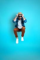 Full length of cheerful young man in casual wear smiling while standing against blue background photo