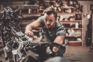 Bike is his life. Confident young man repairing motorcycle in repair shop photo