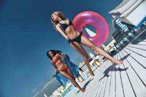 tiempo de diversión en la piscina. Longitud total de dos hermosas mujeres jóvenes en bikini sonriendo mientras corren juntas cerca de la piscina foto