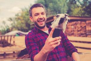 Selfie with llama. Cheerful young man making selfie with llama on his smart phone while standing in the zoo photo