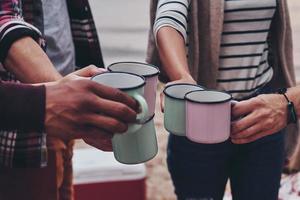 Close up of young people in casual wear toasting each other with mugs while enjoying camping photo