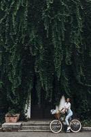 Live green. Full length of attractive young woman in casual wear smiling while standing in front of the house covered with ivy photo