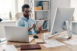 Focusing on the project. Young modern businessman working using digital tablet while sitting in the office photo