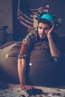 Last night was so intense Handsome young man in beer hat lying on bean bag in messy room after party photo