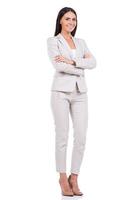 Successful businesswoman. Full length of confident young businesswoman in suit keeping arms crossed and smiling while standing against white background photo