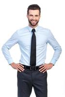 Confident and successful. Confident young handsome man in shirt and tie holding hands on hip and smiling while standing against white background photo