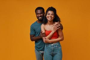 Beautiful young African couple smiling and embracing while standing against yellow background photo