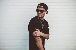 Cool and handsome. Handsome young African man in headphones looking over shoulder while standing in front of the stoned wall outdoors photo