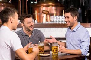 pasar tiempo en el bar. tres alegres amigos bebiendo cerveza en el bar foto