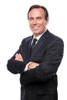 Confident and successful businessman. Waist up of confident mature man in formalwear looking at camera and smiling while keeping arms crossed and standing against white background photo