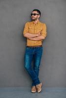 Confident and handsome. Full length of confident mature man in sunglasses keeping arms crossed and looking away while standing against grey background photo