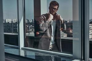 estilo perfecto a través de la foto de la ventana de un apuesto joven con anteojos ajustando su chaqueta mientras camina al aire libre