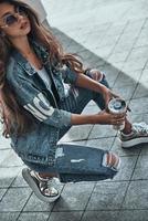Carefree beauty. Attractive young woman in jeans wear holding a disposable cup while crouching outdoors photo