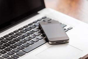 Smart technologies. Close-up of laptop with mobile phone laying on the wooden desk photo