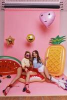 Just relaxing. Two beautiful young women smiling while sitting on the inflatable ring against pink background photo