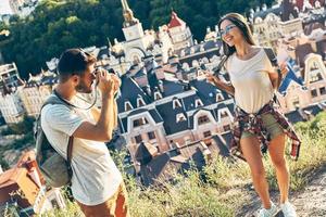 apuesto joven fotografiando a su novia mientras está de pie en la cima de la colina foto