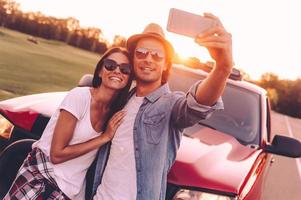 Beautiful young couple bonding to each other and leaning at their pick-up truck while making selfie photo