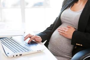 Pregnant woman working on laptop. Cropped image of pregnant businesswoman typing something on laptop while sitting at her working place in office photo