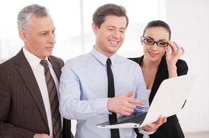 trabajando juntos en un proyecto. tres empresarios confiados discutiendo algo mientras miran la computadora portátil foto